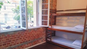 Une chambre avec des lits superposés, un mur en briques et une fenêtre donnant sur la rue.