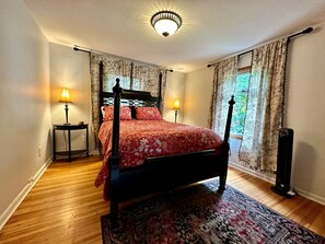 A bedroom with a four-poster bed, two bedside lamps, floral curtains, and a view of greenery outside. - Seattle's Starlight Bungalow  (Seattle)