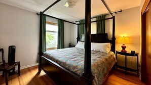 Ein Himmelbett mit floralem Überwurf, ein Nachttisch mit Lampe und ein Sessel.