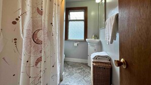 Ein Badezimmer mit Duschvorhang, Fenster, Waschbecken und Spiegel.