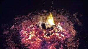Ein Lagerfeuer mit Baumstämmen und einer Metalltasse in der Mitte, umgeben von Steinen.