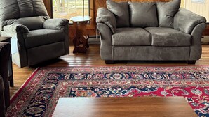 Ein gemütliches Wohnzimmer mit zwei grauen Sofas, einem gemusterten Teppich und einem Holztisch.
