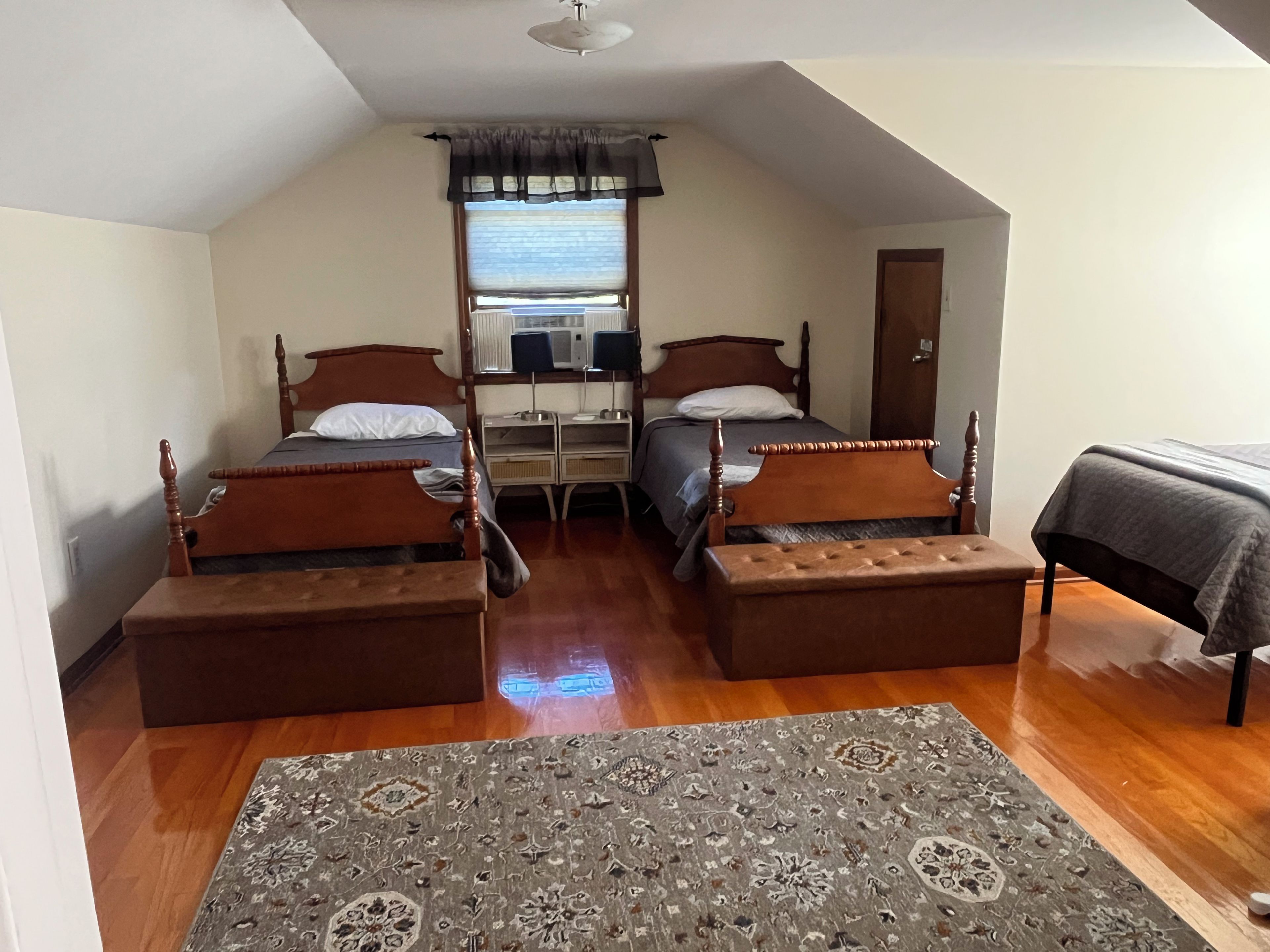 Une chambre avec deux lits en bois, un bureau avec un ordinateur et un tapis à motifs.