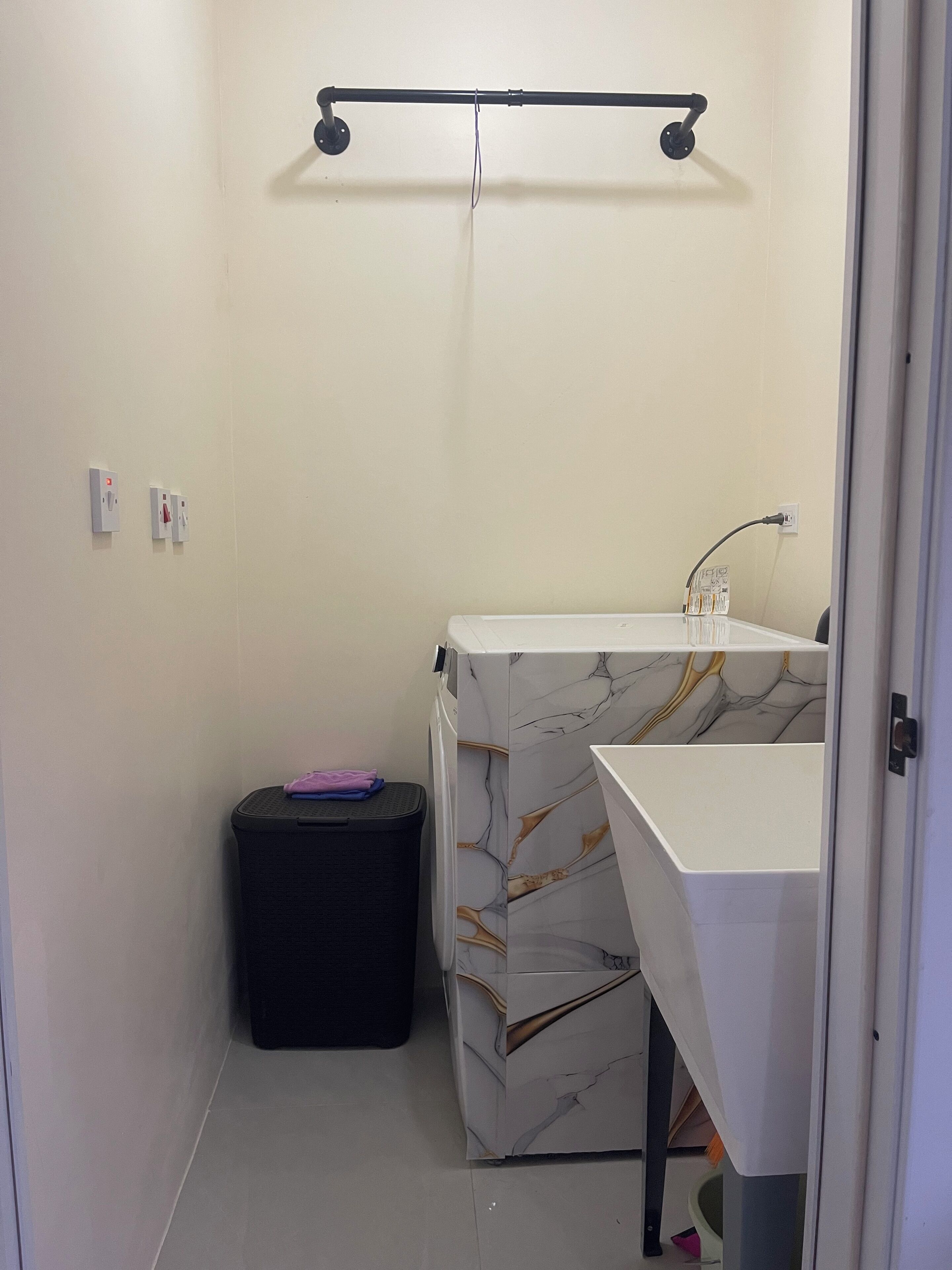 Une petite salle de bain avec un lavabo blanc, une poubelle noire et un meuble-lavabo à motifs de marbre.