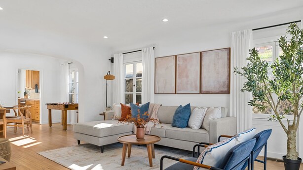 A modern living room with a sofa, coffee table, and chairs. There is a dining area with a table and chairs. A large window provides natural light. - Steps to Beach & 2nd St. Retreat, Hot-Tub, Parking, 3BR w/Private Studio (Long Beach)