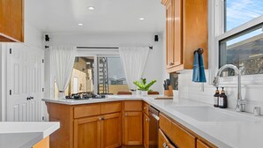 A modern kitchen with wooden cabinets, a white countertop, and a large window. - Steps to Beach & 2nd St. Retreat, Hot-Tub, Parking, 3BR w/Private Studio (Long Beach)