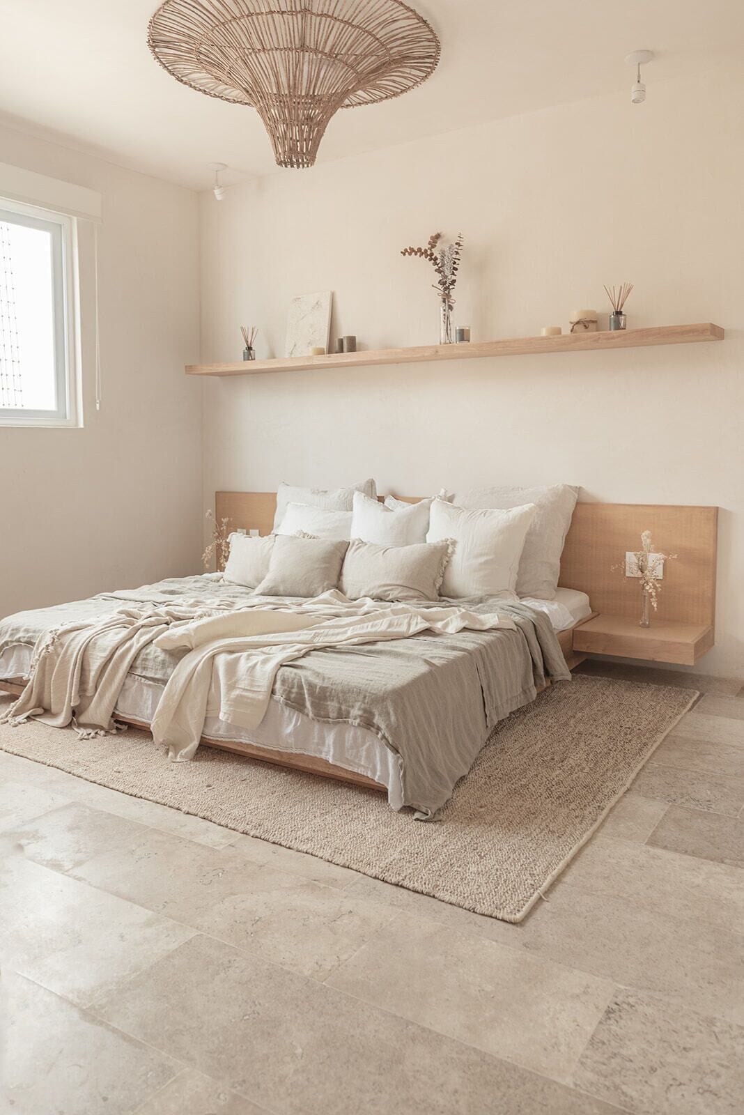 A bedroom with a large bed, a wooden headboard, a woven light fixture, and a small shelf with decorative items.