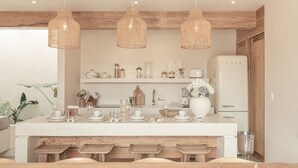 Een moderne keuken met een centraal kookeiland, houten barkrukken, hangende rieten lampen en een witte koelkast.