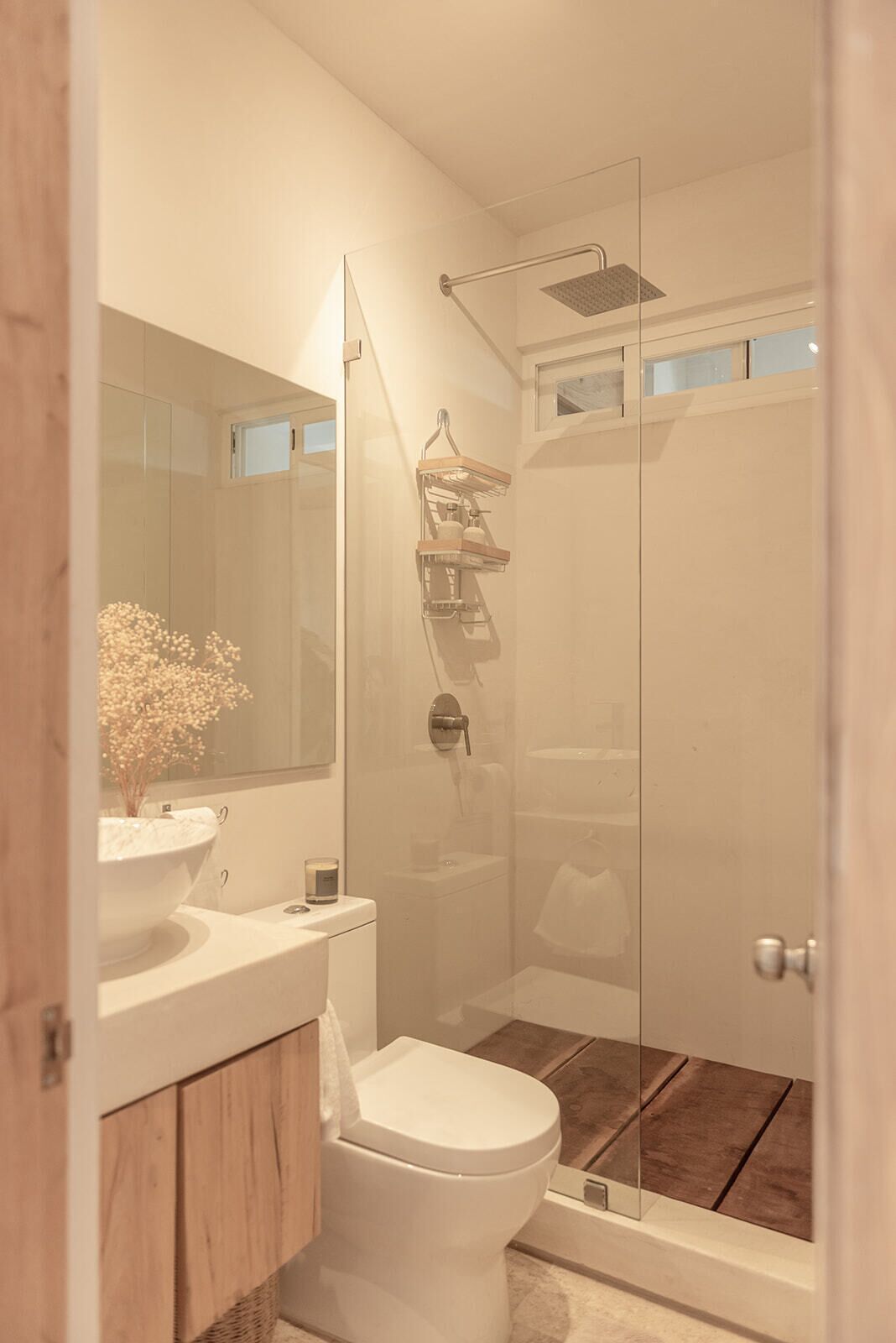 Een moderne badkamer met een douchecabine van glas, een wit toilet, een houten wastafelmeubel en een grote spiegel.