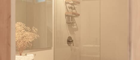 Een moderne badkamer met een douchecabine van glas, een wit toilet, een houten wastafelmeubel en een grote spiegel.
