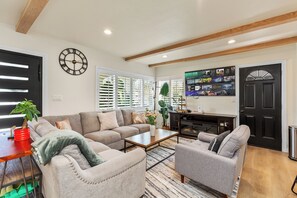 Ein Wohnzimmer mit einer Couch, Sesseln, einem Couchtisch und einer TV-Wand.