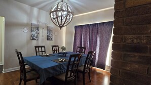 Uma sala de jantar com toalha de mesa azul, cadeiras de madeira, um candelabro e obras de arte nas paredes.