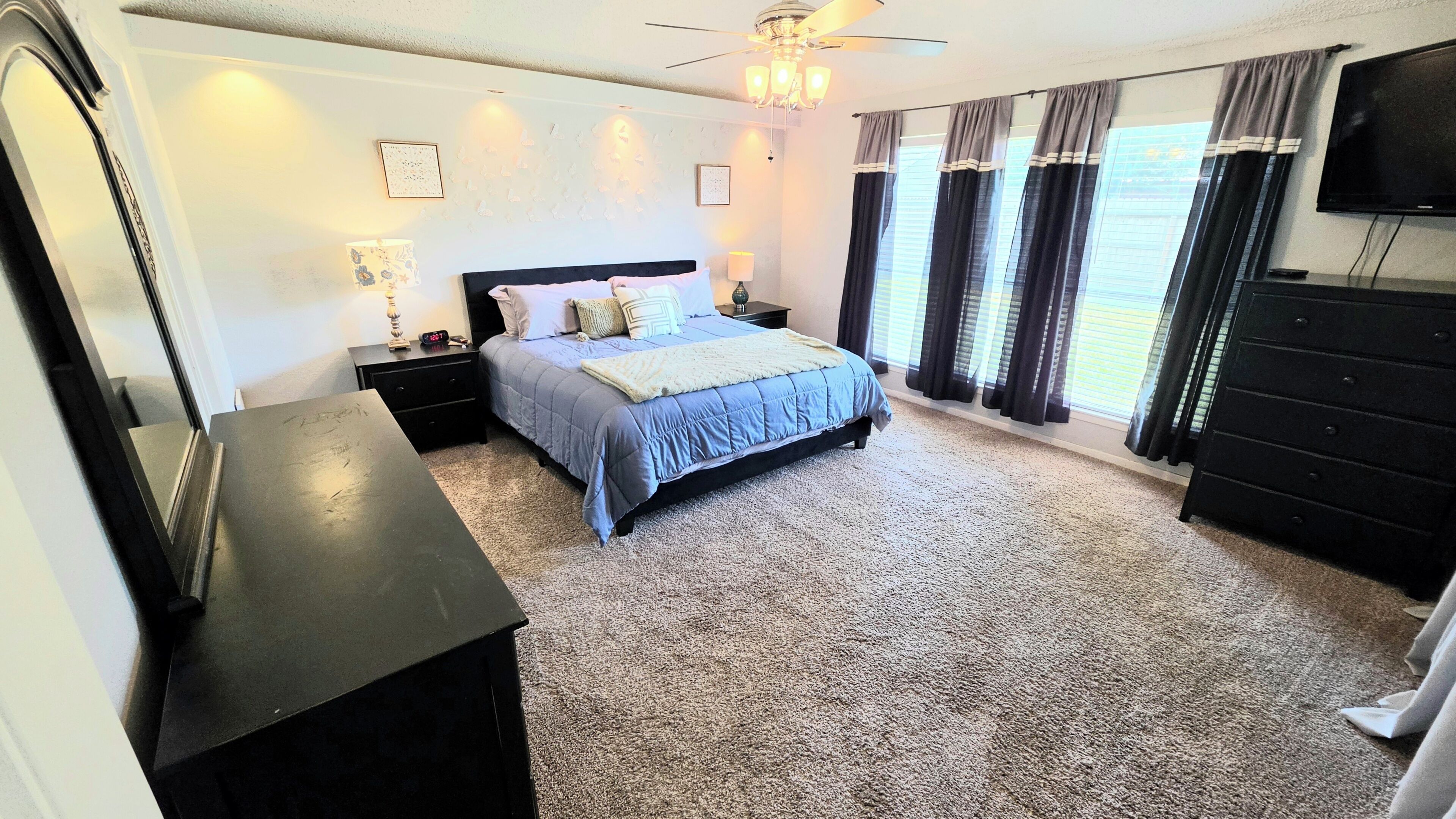 Une chambre à coucher comprenant un lit, des tables de chevet, une commode, un ventilateur de plafond et un téléviseur.