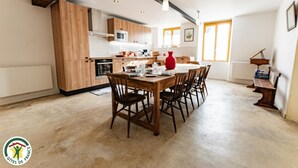 Moderni keittiö, jossa on puiset kaapit, ruokapöytä tuoleineen ja punainen maljakko.