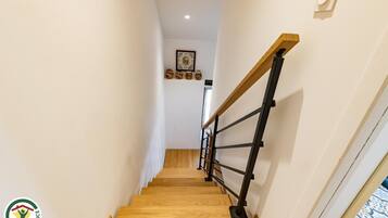 Un escalier en bois avec une rampe noire, menant à un palier orné d’un tableau encadré et d’objets décoratifs.