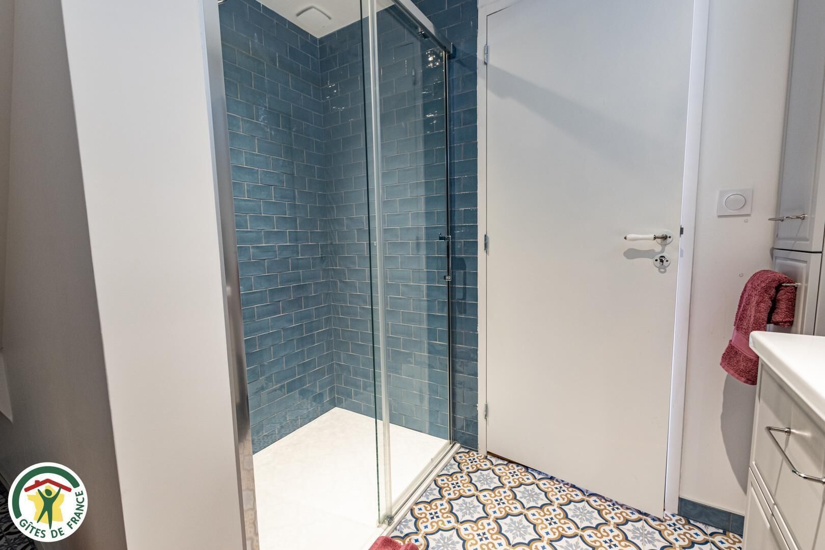 A bathroom with a glass shower enclosure, a white sink, and a patterned floor.