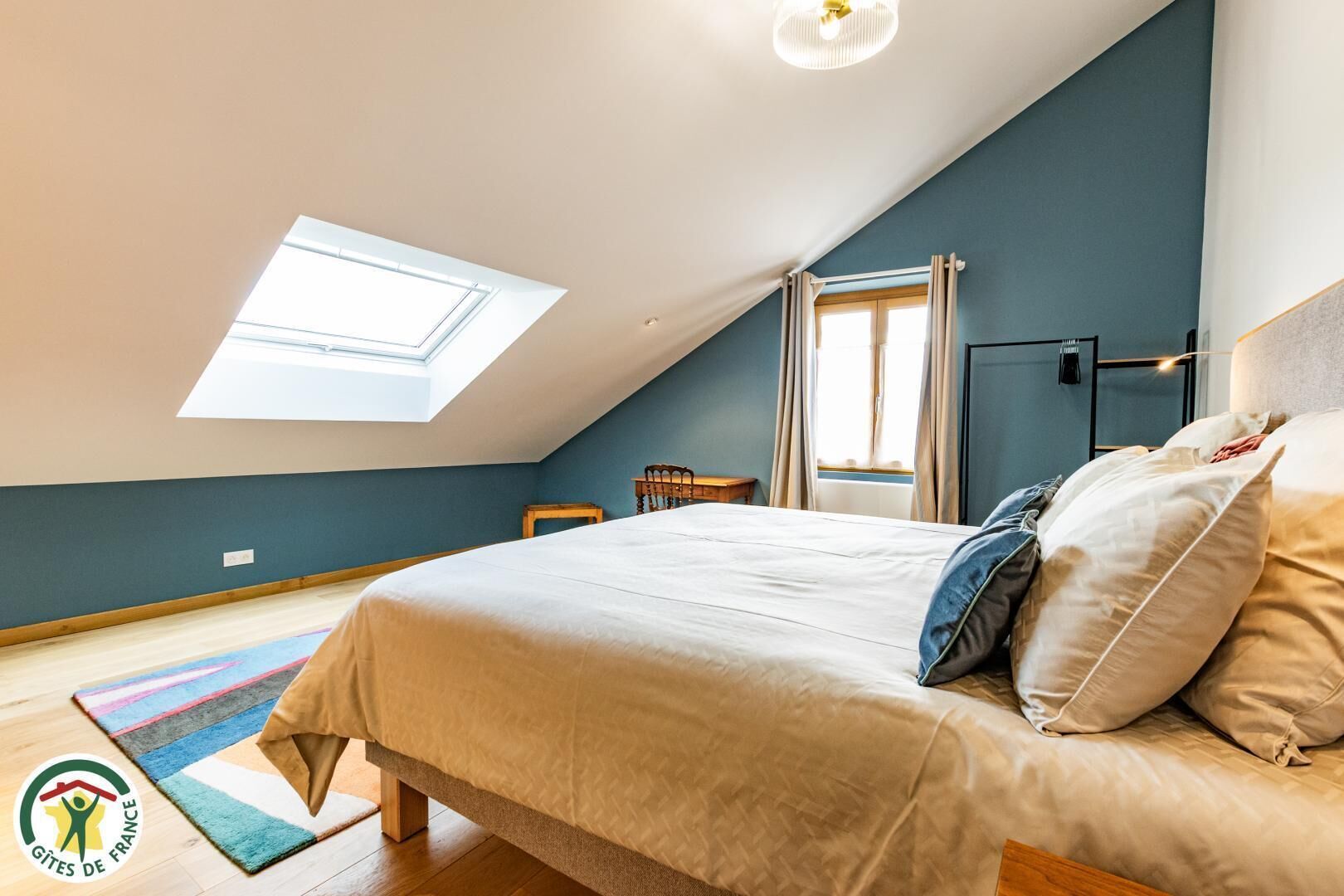 Ein Schlafzimmer mit Dachfenster, einem Bett mit Kissen, einem Fenster und einem kleinen Tisch.