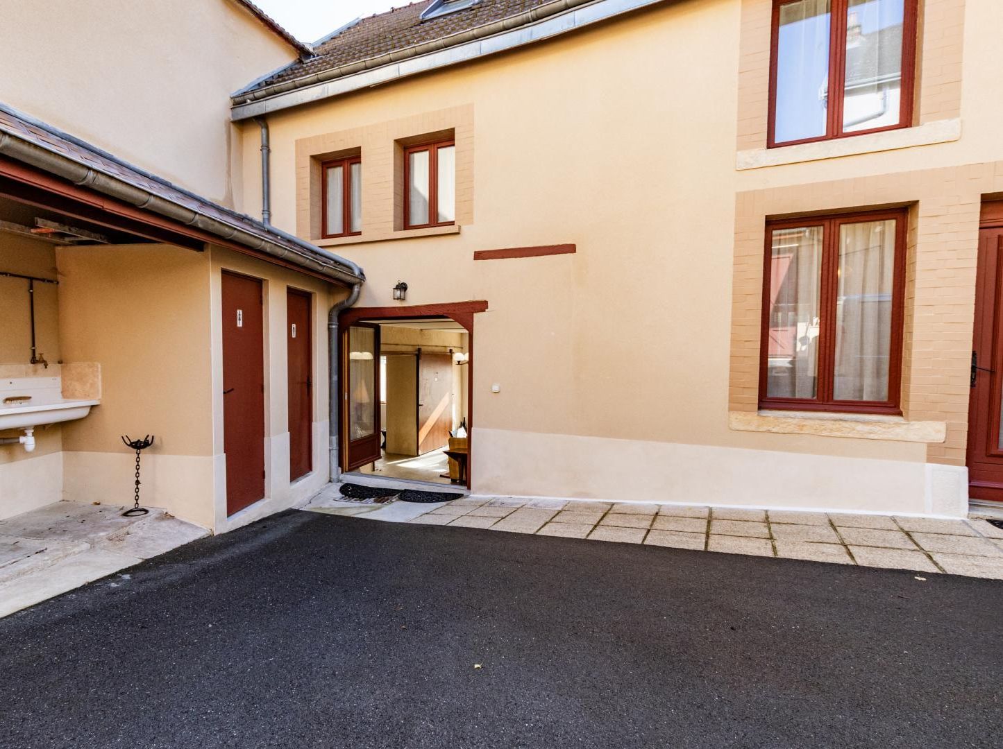 Un bâtiment doté d’une cour dallée, d’un évier à l’extérieur et d’une porte donnant sur un espace intérieur.