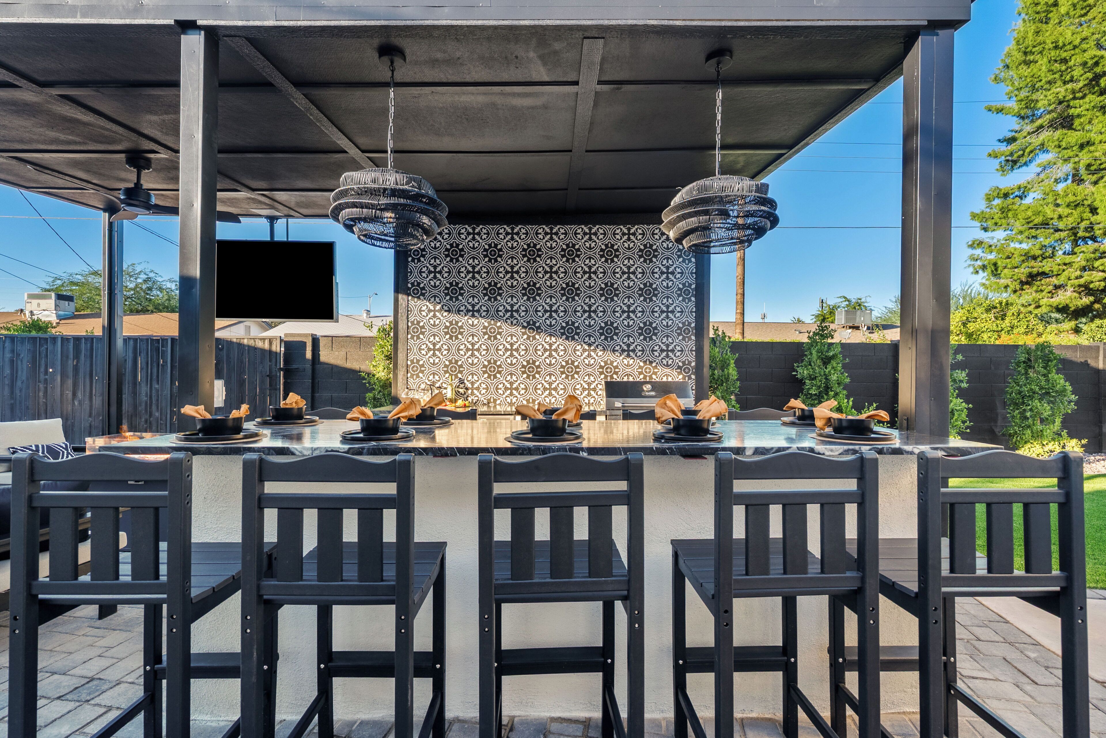 An outdoor dining area with a patterned wall, black chairs, and a flat-screen TV.