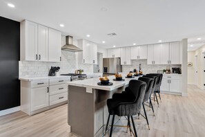 A modern kitchen with white cabinetry, a central island with bar stools, and a stainless steel refrigerator. - Group Getaway - Heated Pool, Hot Tub, Casita, Outdoor Bar, Games & Jazz Lounge (Scottsdale)