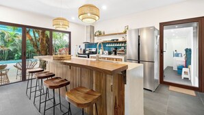 Eine moderne Küche mit einer Holzbar, Edelstahlgeräten und Blick auf einen tropischen Garten.