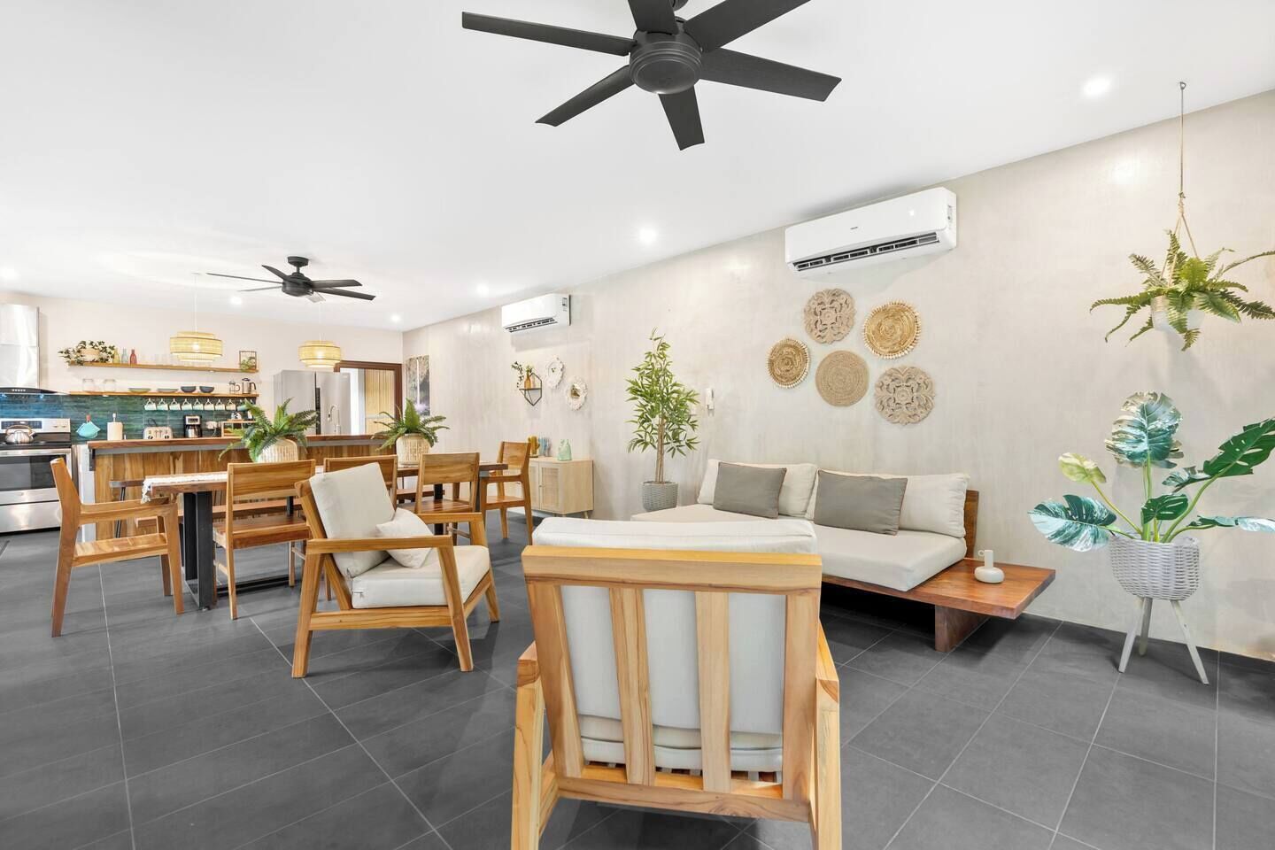Una sala de estar moderna con un sofá, sillas de madera, un comedor con mesa y sillas, y una cocina al fondo.