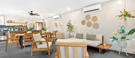 Una sala de estar moderna con un sofá, sillas de madera, un comedor con mesa y sillas, y una cocina al fondo.