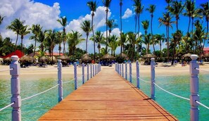 A wooden pier leading to a beach with palm trees and thatched umbrellas. - Private Pool Villa in Gated Casa Linda, Near Sosua Beaches (Sosúa)