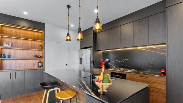 Una cocina moderna con armarios de madera oscura, encimera de mármol e iluminación colgante.