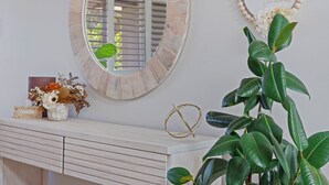 Un tocador de baño con un espejo redondo, un adorno en la pared y una planta en maceta.