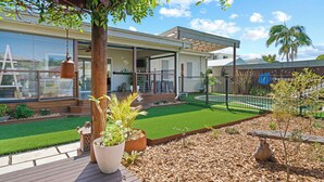 Una casa moderna con un porche cubierto, un patio trasero cercado y un césped bien cuidado.