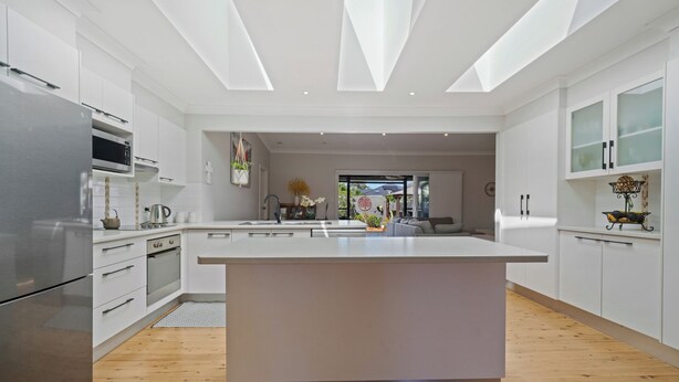Una cocina moderna con armarios blancos, una isla central y un amplio ventanal que proporciona luz natural.