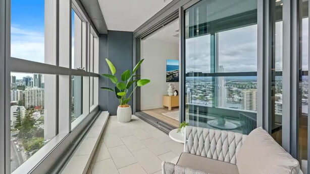Un balcon moderne offrant une vue sur la ville, agrémenté d’une plante en pot et d’un coin salon avec un fauteuil confortable.