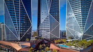 Un hôtel moderne doté d’une architecture géométrique originale, avec un espace piscine central entouré de palmiers et de chaises longues.