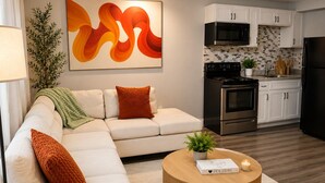 Una sala de estar moderna con un sofá seccional, una mesa de centro redonda, una mesita auxiliar y una cocina al fondo.