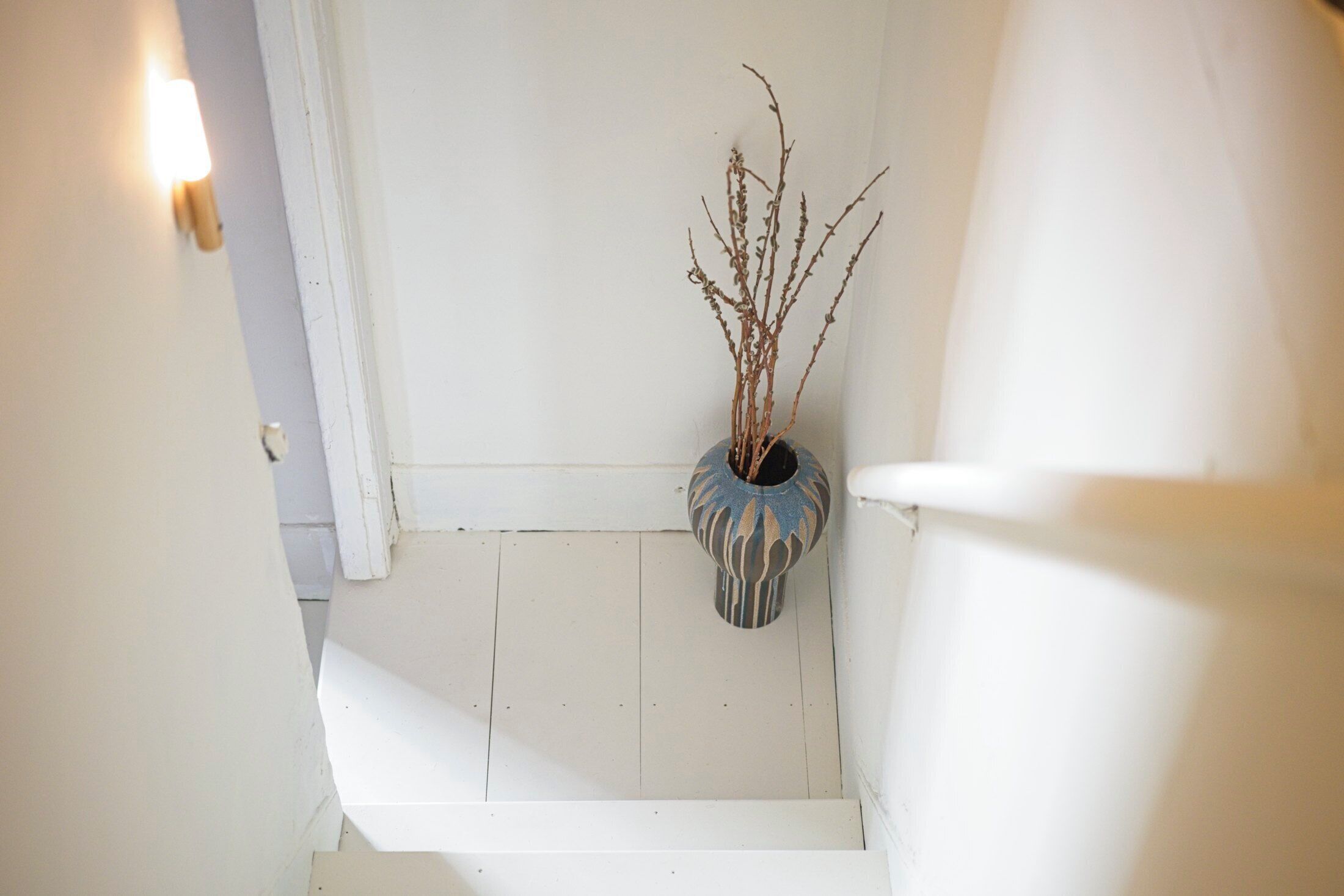 A staircase with a white railing and a decorative vase with branches on the wall.