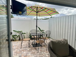 A patio with a table and chairs, an umbrella, and a wicker sofa. - Walk to Bustling Downtown Delray Beach (Delray Beach)