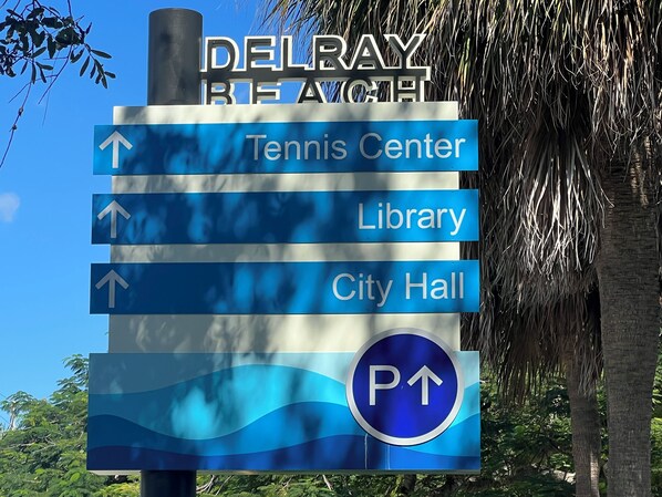 A directional sign with arrows pointing to Tennis Center, Library, City Hall, and a parking area. - Walk to Bustling Downtown Delray Beach (Delray Beach)