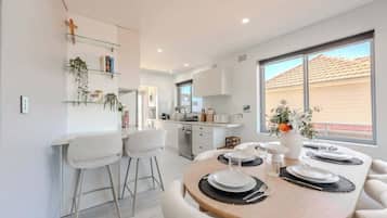 A modern kitchen with white cabinets, a dining area with a round table set for four, and a large window providing a view of the outside.