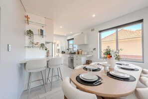 Una cocina moderna con armarios blancos, un comedor con una mesa redonda para cuatro personas y un ventanal que ofrece vistas al exterior.