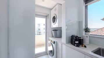 A compact kitchen with a built-in washer and dryer, a coffee machine, and a view through a window.