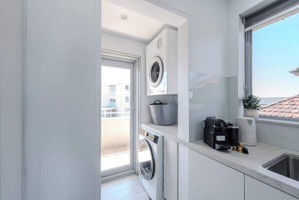 Cocina compacta con lavadora y secadora integradas, cafetera y vistas al exterior.