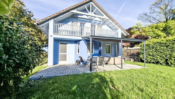 A two-story house with a balcony, a covered patio area, and a well-maintained garden.