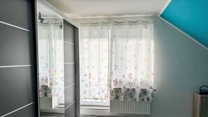 A bedroom with a large window, a radiator, and a mirror.