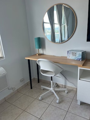A modern office space with a wooden desk, a white office chair, a round mirror, and a teal lamp. - Beachfront 3-Bedroom Apartment with Breathtaking Views in Luquillo (Luquillo)