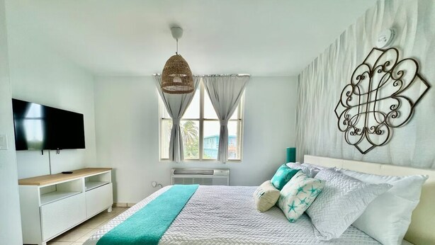 A bedroom with a bed, a TV, a window with curtains, and a wall decoration. - Beachfront 3-Bedroom Apartment with Breathtaking Views in Luquillo (Luquillo)