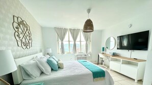 A bedroom with a bed, a TV, a desk, and a window with curtains. - Beachfront 3-Bedroom Apartment with Breathtaking Views in Luquillo (Luquillo)