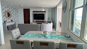 A dining area with a table set for four, grey upholstered chairs, a teal table runner, and a bowl of decorative items on the table. - Beachfront 3-Bedroom Apartment with Breathtaking Views in Luquillo (Luquillo)