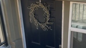 Una puerta negra con un adorno de lazo, una ventana con persianas y una barandilla de metal.