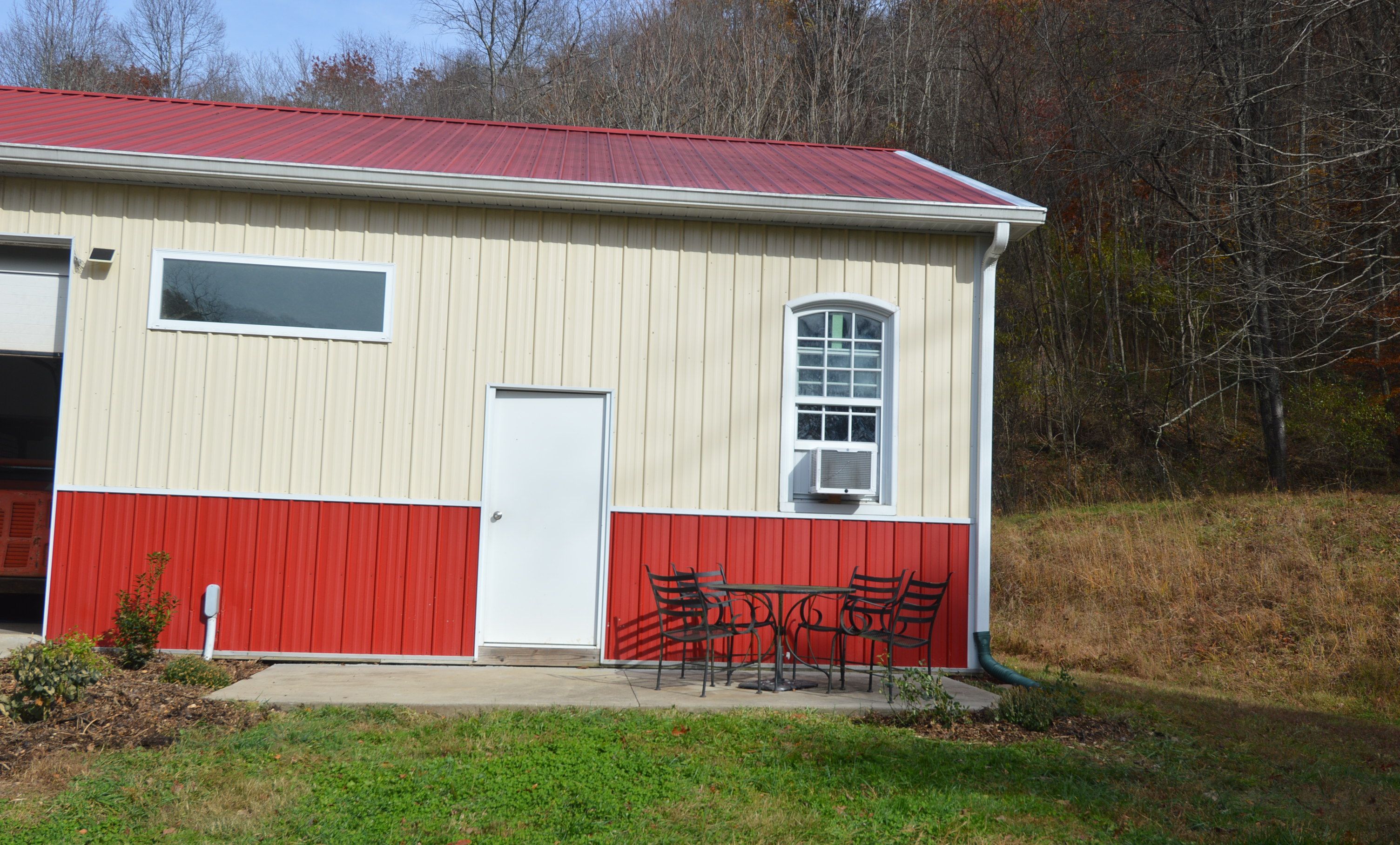 A single-story building with a red and white exterior, a door, a window, and a small outdoor seating area with metal chairs.
